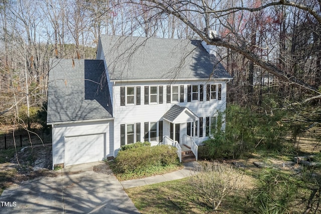 colonial home featuring a garage, roof with shingles, and driveway