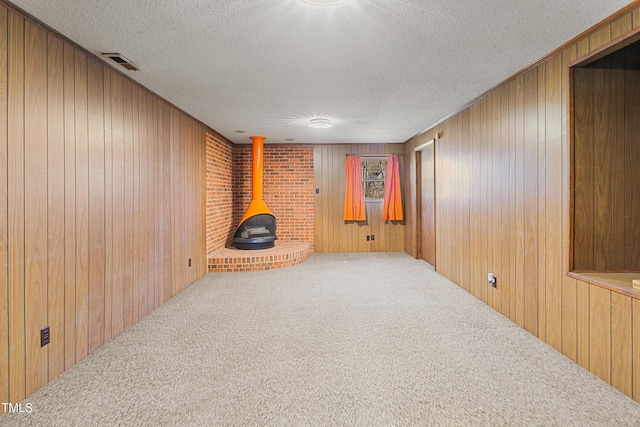 carpeted living room with visible vents, wooden walls, a wood stove, and a textured ceiling