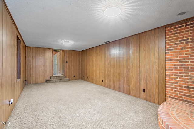 carpeted spare room featuring wood walls and a textured ceiling