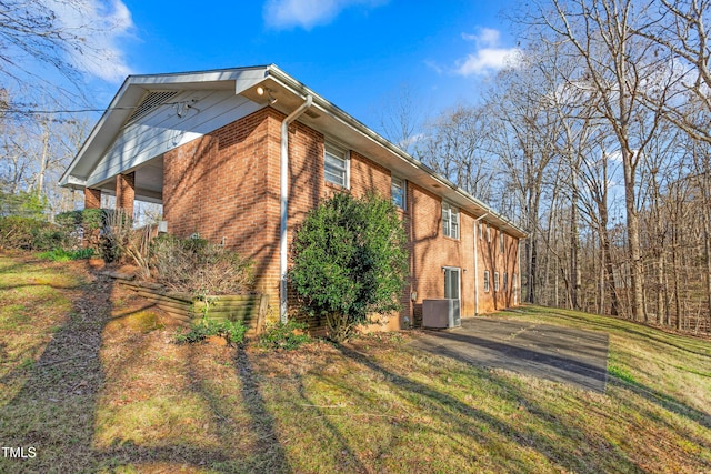 view of side of home featuring brick siding, cooling unit, and a yard