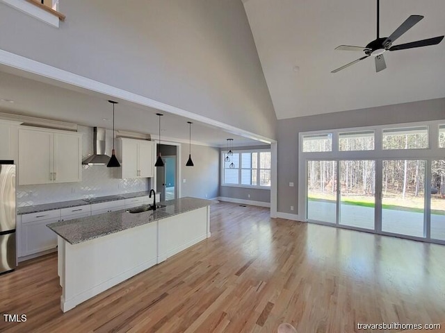 kitchen featuring wall chimney range hood, stone counters, freestanding refrigerator, black electric cooktop, and a sink