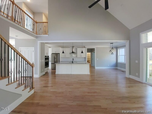 unfurnished living room featuring baseboards, stairs, a high ceiling, light wood-style floors, and a sink