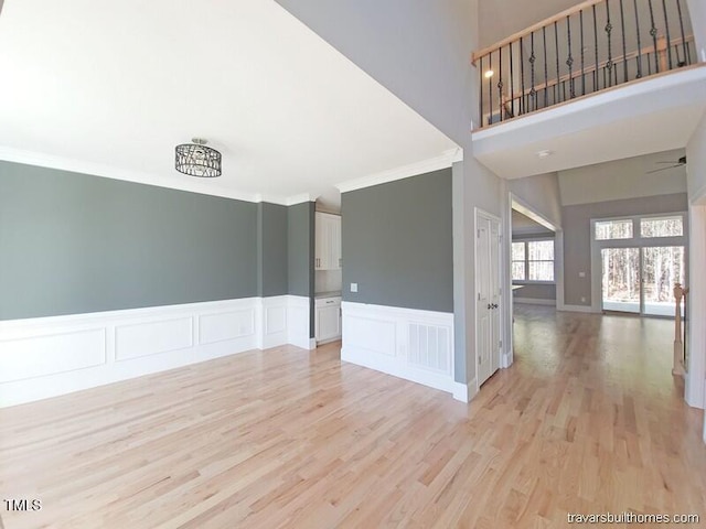 empty room with visible vents, light wood-style floors, ornamental molding, and a ceiling fan