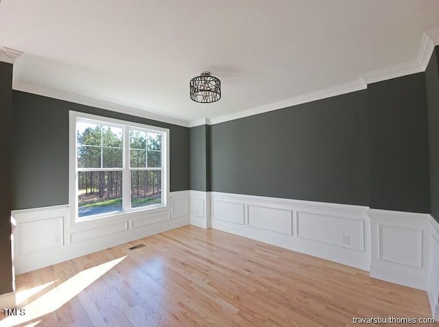 spare room featuring crown molding, light wood-style floors, visible vents, and wainscoting