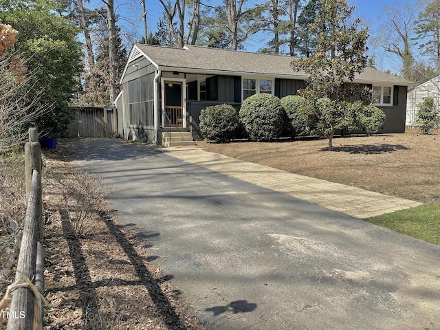 view of front facade with board and batten siding, a shingled roof, driveway, and fence