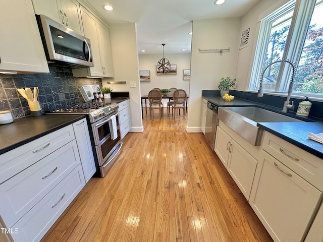 kitchen featuring a sink, dark countertops, tasteful backsplash, stainless steel appliances, and light wood-style floors