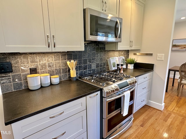 kitchen with dark countertops, tasteful backsplash, light wood-style floors, appliances with stainless steel finishes, and baseboards