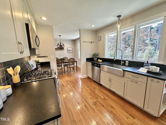 kitchen featuring dark countertops, light wood finished floors, pendant lighting, appliances with stainless steel finishes, and a sink