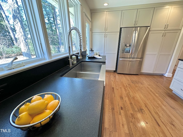 kitchen with a sink, dark countertops, light wood-style flooring, and stainless steel fridge with ice dispenser