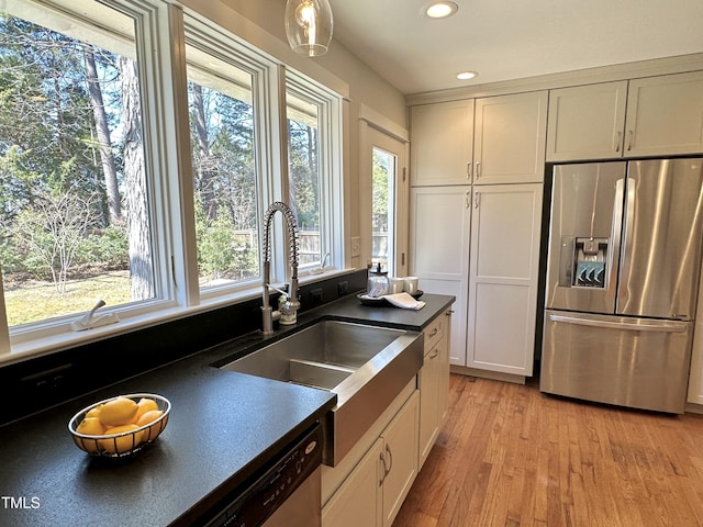 kitchen featuring light wood-style flooring, a sink, dark countertops, recessed lighting, and stainless steel appliances