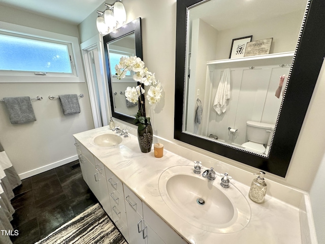 bathroom featuring double vanity, toilet, baseboards, and a sink