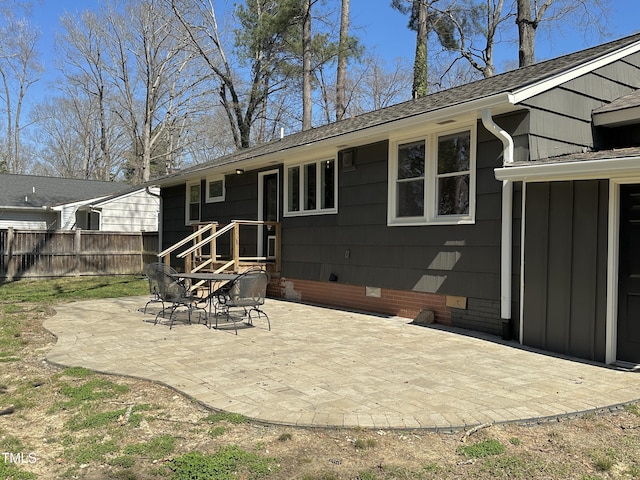 rear view of property with crawl space, fence, roof with shingles, and a patio area