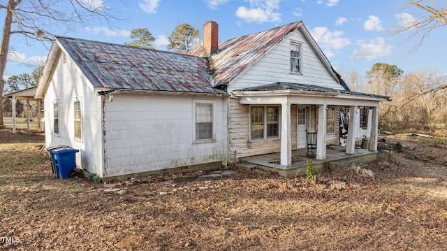 rear view of house featuring covered porch, a chimney, and metal roof