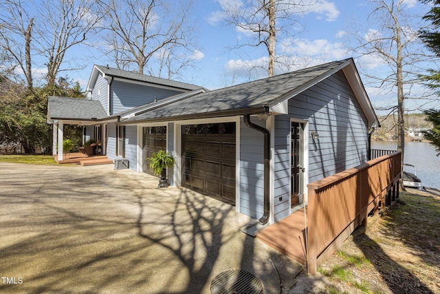 view of property exterior featuring an attached garage, a water view, driveway, and a shingled roof