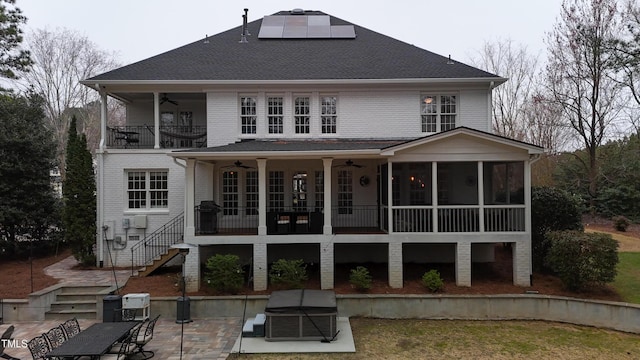 back of house featuring stairway, a sunroom, ceiling fan, a patio area, and roof mounted solar panels