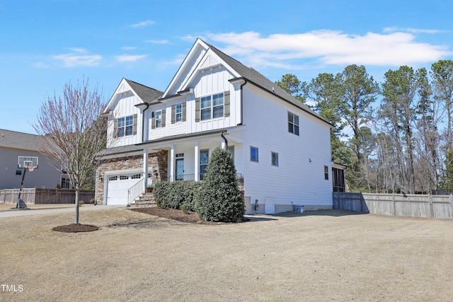 view of front of house with driveway, stone siding, fence, board and batten siding, and a garage