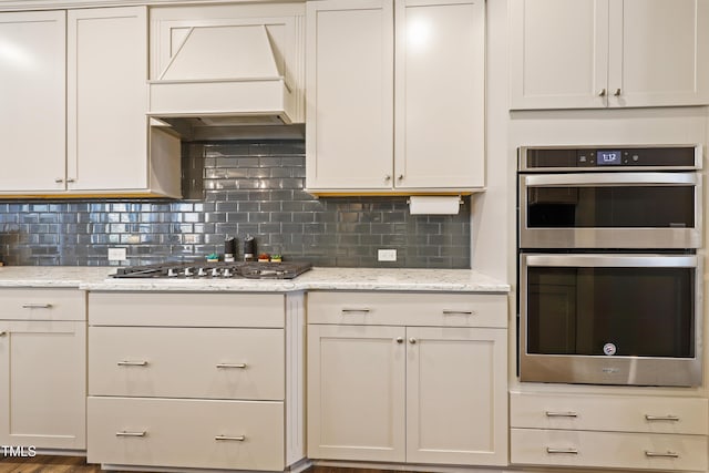 kitchen with custom exhaust hood, backsplash, light stone countertops, and appliances with stainless steel finishes