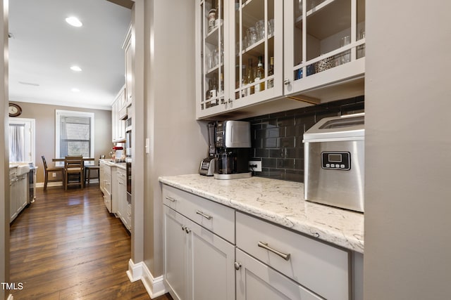 kitchen featuring dark wood-type flooring, ornamental molding, light stone counters, tasteful backsplash, and glass insert cabinets