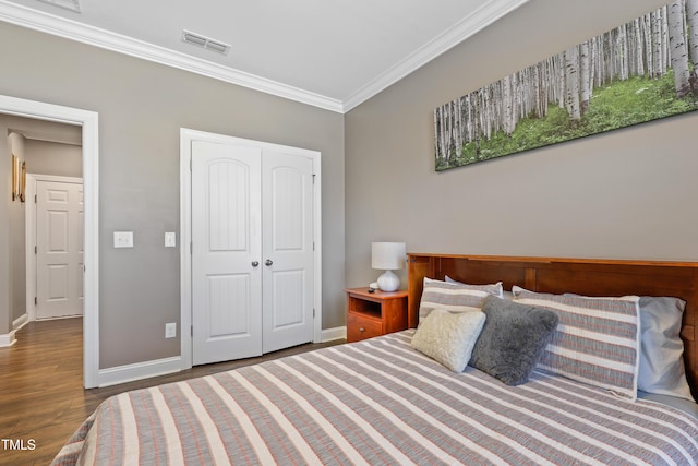 bedroom featuring wood finished floors, visible vents, baseboards, a closet, and crown molding