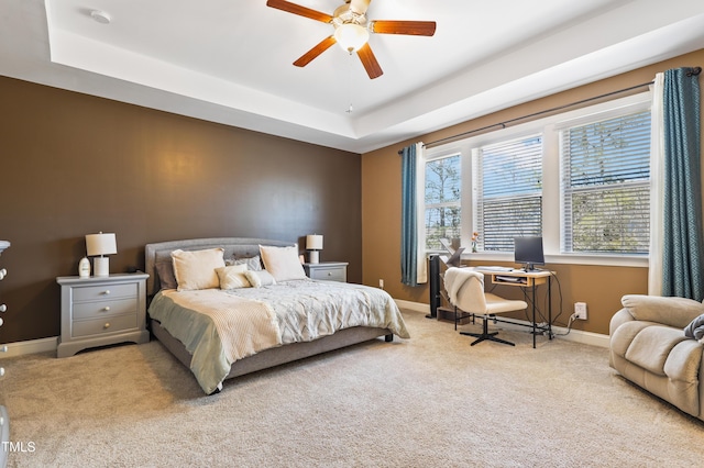 carpeted bedroom featuring ceiling fan, a raised ceiling, and baseboards