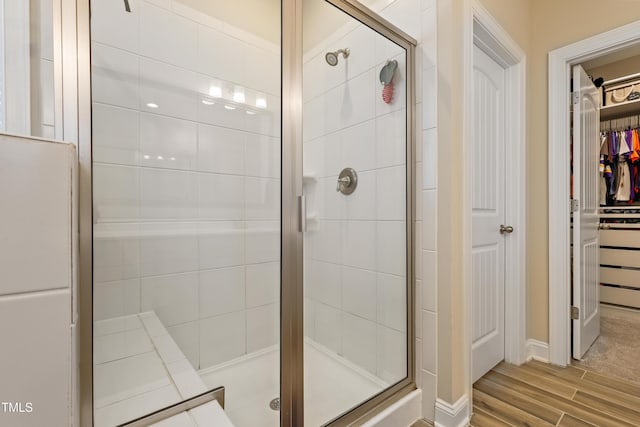 bathroom with a walk in closet, wood finished floors, and a shower stall