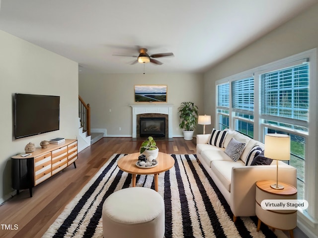 living room featuring baseboards, a fireplace with flush hearth, stairs, wood finished floors, and a ceiling fan