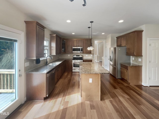 kitchen featuring tasteful backsplash, light stone counters, wood finished floors, stainless steel appliances, and a sink