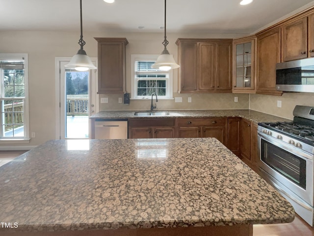 kitchen with a sink, dark stone countertops, a kitchen island, stainless steel appliances, and glass insert cabinets