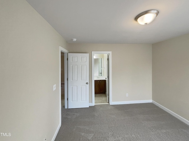 unfurnished bedroom featuring ensuite bathroom, baseboards, and dark carpet