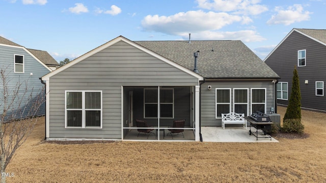 back of property with a sunroom, a lawn, roof with shingles, and a patio area