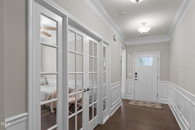 doorway featuring dark wood finished floors, ornamental molding, wainscoting, french doors, and a decorative wall