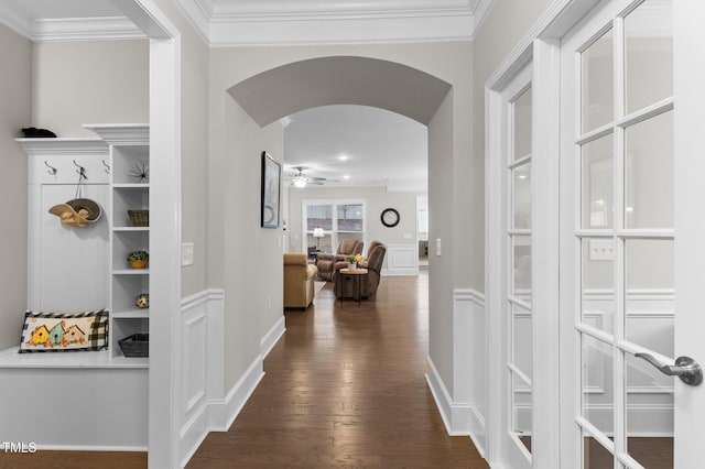 hallway with arched walkways, dark wood-type flooring, ornamental molding, and a decorative wall