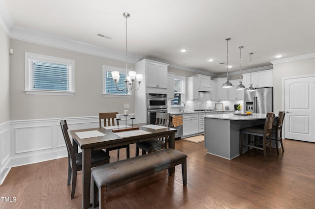 dining room featuring visible vents, dark wood-type flooring, a wainscoted wall, ornamental molding, and an inviting chandelier