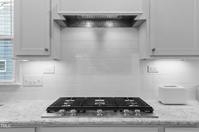 kitchen featuring tasteful backsplash, under cabinet range hood, light stone counters, stainless steel gas stovetop, and white cabinets