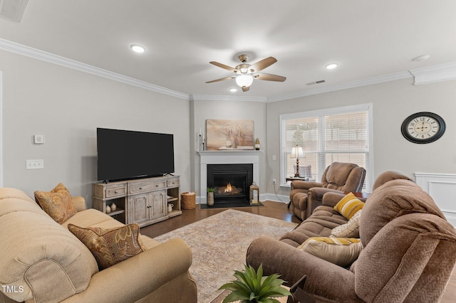 living area featuring visible vents, a fireplace with flush hearth, a ceiling fan, and ornamental molding