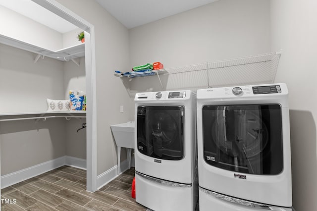 clothes washing area featuring washing machine and clothes dryer, laundry area, baseboards, and wood tiled floor