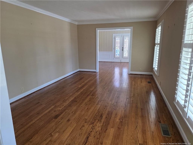 spare room featuring visible vents, baseboards, crown molding, and dark wood-type flooring