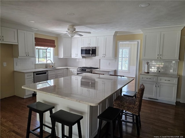 kitchen featuring dark wood finished floors, a sink, white cabinets, appliances with stainless steel finishes, and a kitchen breakfast bar