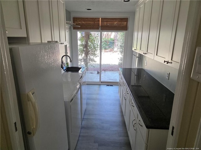 kitchen featuring a sink, white refrigerator with ice dispenser, wood finished floors, white cabinetry, and separate washer and dryer