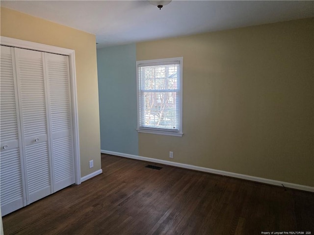 unfurnished bedroom featuring a closet, baseboards, visible vents, and dark wood-style flooring