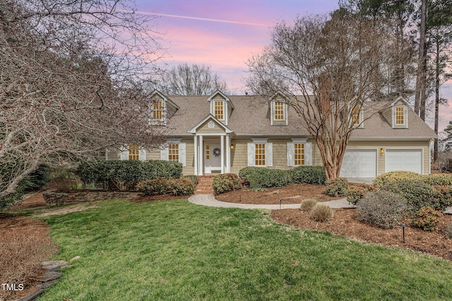 new england style home with a front yard, an attached garage, and roof with shingles