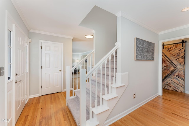 stairs featuring a barn door, wood finished floors, baseboards, and ornamental molding