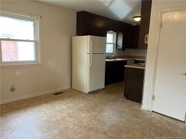 kitchen with visible vents, baseboards, light floors, freestanding refrigerator, and a sink