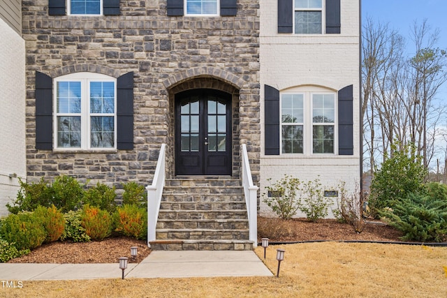 entrance to property with crawl space, stone siding, french doors, and brick siding