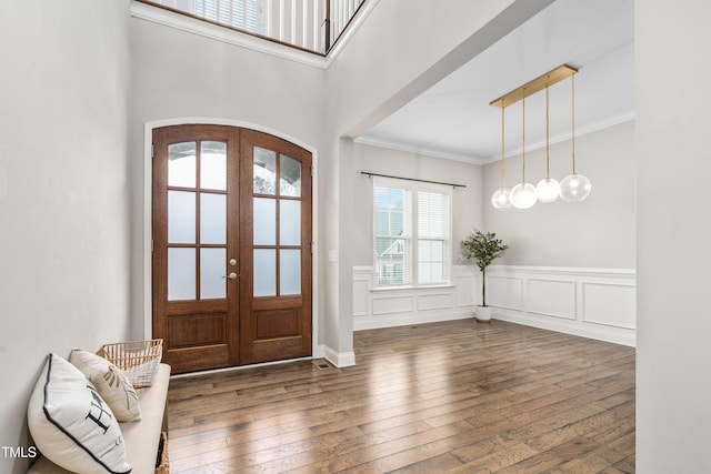 foyer with a wainscoted wall, arched walkways, hardwood / wood-style flooring, french doors, and crown molding