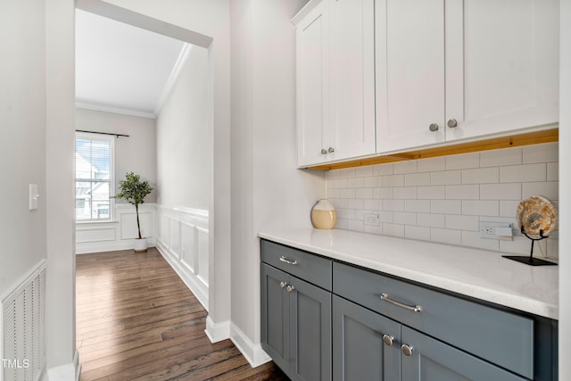 interior space featuring visible vents, dark wood-type flooring, ornamental molding, tasteful backsplash, and wainscoting