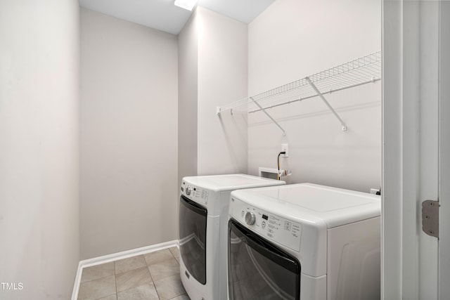 clothes washing area with light tile patterned floors, baseboards, independent washer and dryer, and laundry area