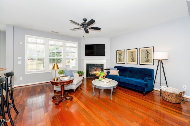 living area featuring a high end fireplace, baseboards, ceiling fan, and wood-type flooring