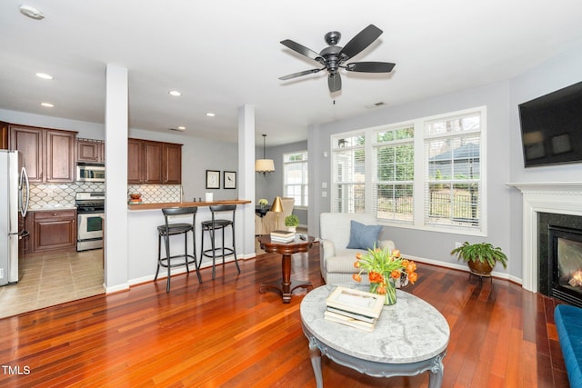 living area featuring wood finished floors, visible vents, baseboards, ceiling fan, and a glass covered fireplace