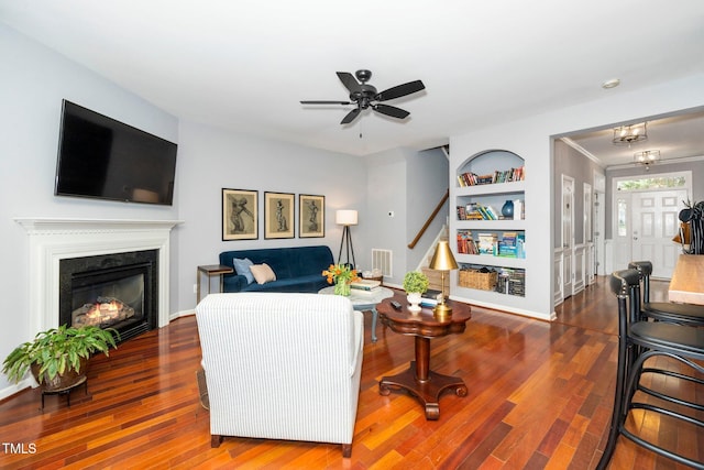 living room with built in features, wood finished floors, visible vents, ceiling fan, and a glass covered fireplace